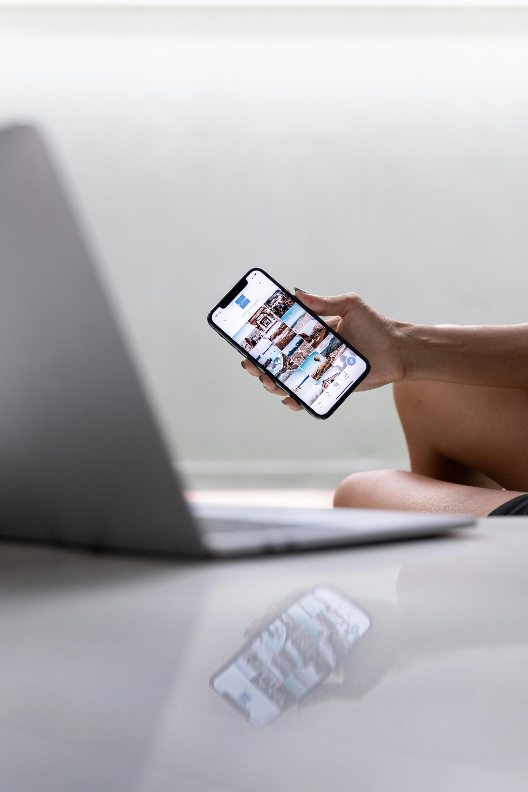 A woman multitasks using a smartphone and laptop for social media in a modern setting.